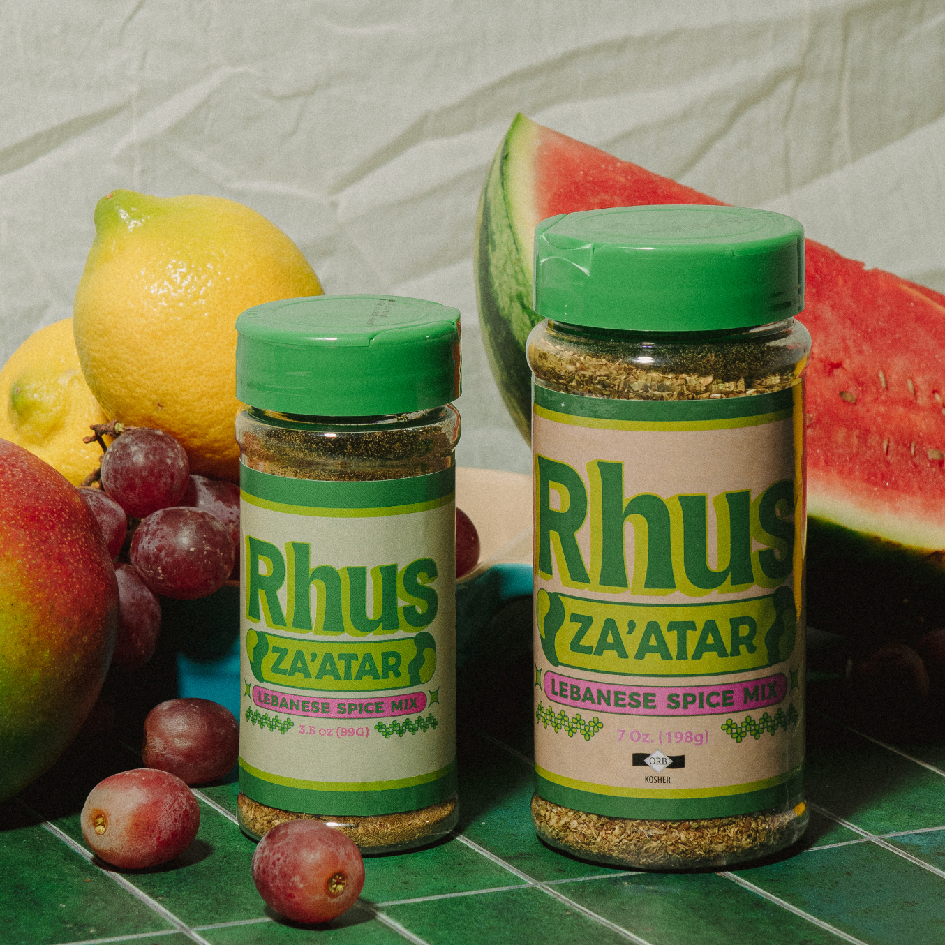 Za'atar small and large canisters photographed in front of an arrangement of fruit 